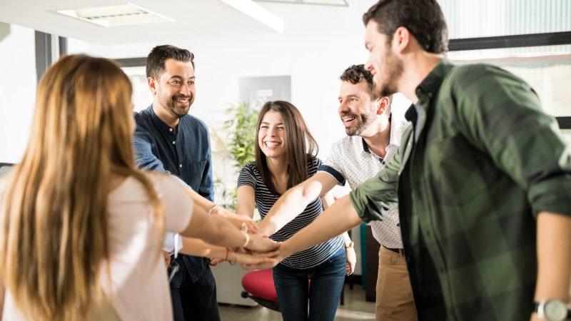 Equipe de salariés souriants qui ont les mains posées les unes sur les autres