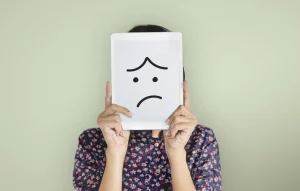 Image d'une personne qui tient un feuille avec un visage triste devant sa tête